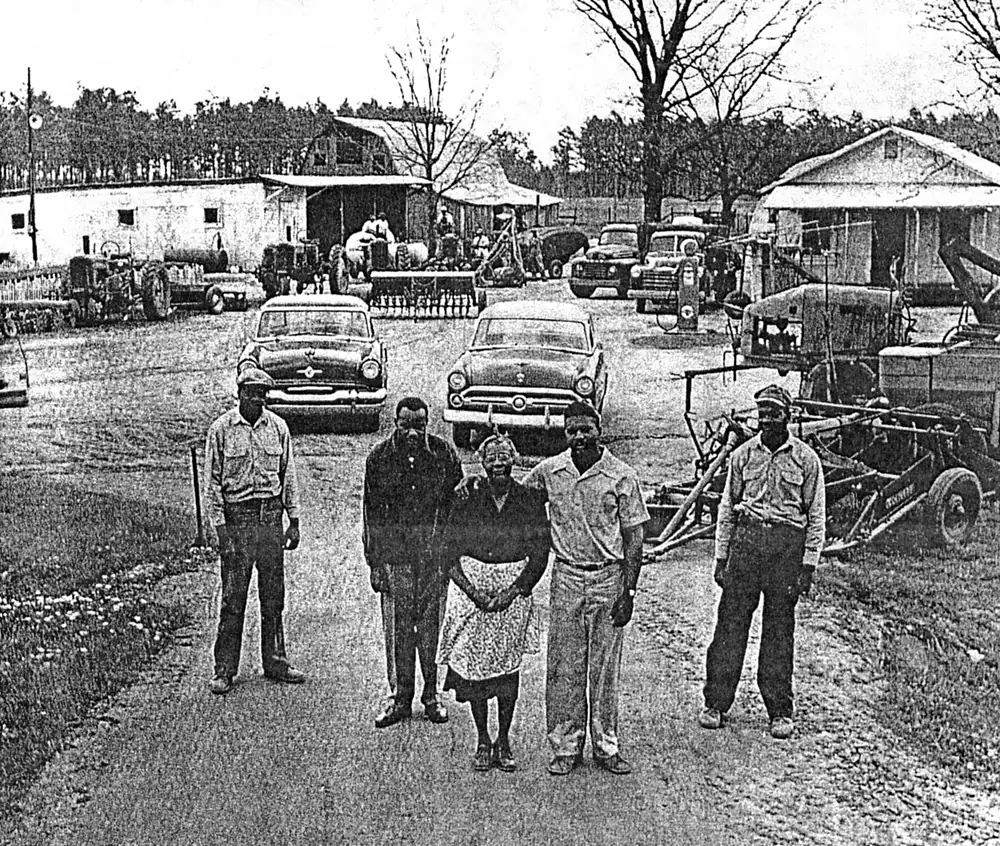 Amelia Jenkins stands with her four grown sons on the dirt road through the family farm, with tractors, trucks, cars and farm buildings ranged behind them.